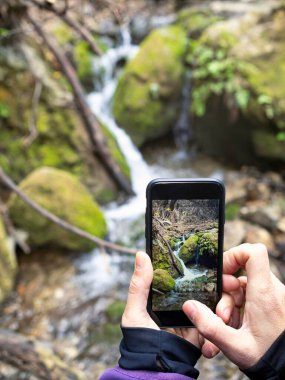 Ormanda şelaleyi fotoğraflayan bir kadının kesilmiş görüntüsü. Yürüyüş ve doğa turizmi.