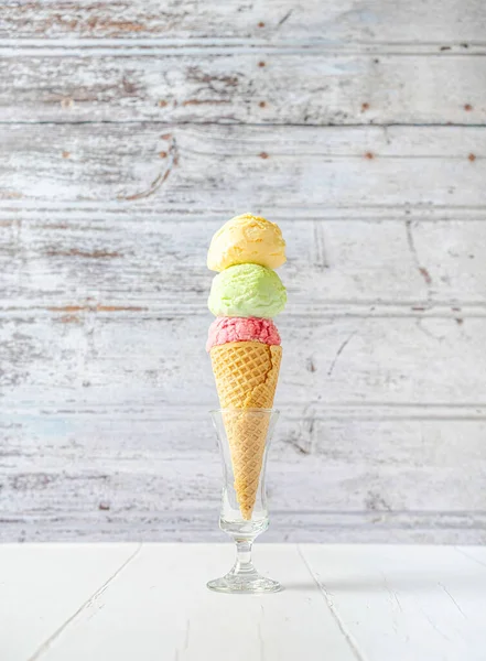Strawberry, vanilla and pistachio ice cream cone in a glass, on a vintage wooden background.
