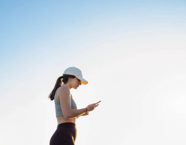 Profil kenarı fotoğrafı. Beyaz şapkalı bir kız cep telefonuna bakıyor..