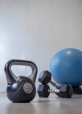 Spor salonunda insanların olmadığı bir oda. Dambıl ve spor topunun yanında dambıllar. Beyaz arka plan ve ahşap zemin. Sağlıklı yaşam tarzı