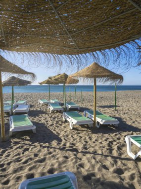 İspanya 'nın Torremolinos plajında güneş şezlonglu saman plajı şemsiyeleri. Arka planda mavi gökyüzü ve deniz. Yaz tatilleri, yaz tatilleri.