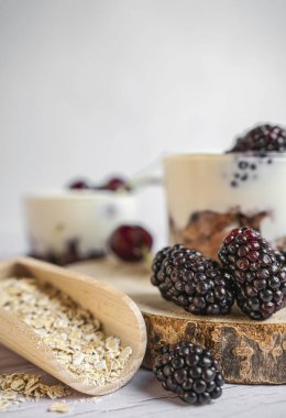 Böğürtlen ve kirazlı yoğurt, yulaflı taze meyve, beyaz ahşap arka plan.