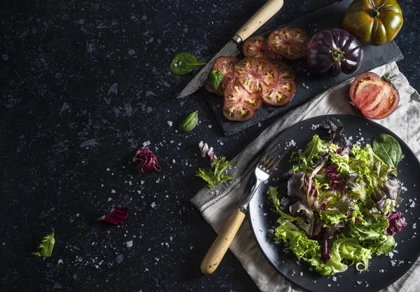 Stock image Tomato salad with spinach, green tomatoes, lettuce, Treviso lettuce and basil. Tomato slices. Homemade food. Concept of a tasty and healthy meal. Dark stone background. Top view. Space for text.