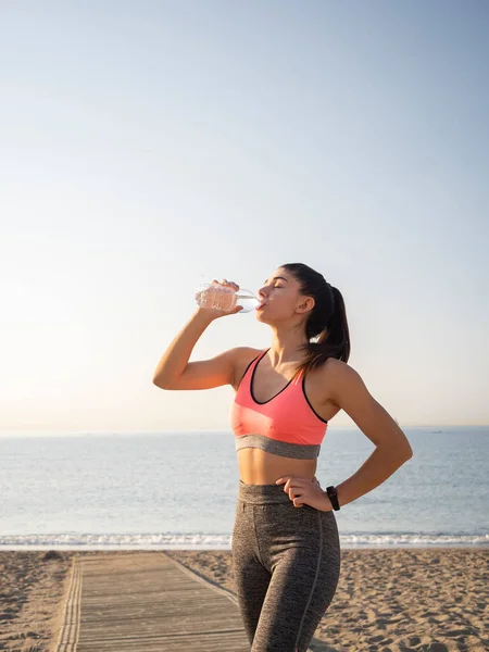 stock image Girl athlete taking a break during the race to hydrate during exercise on the beach. Active and healthy lifestyle.