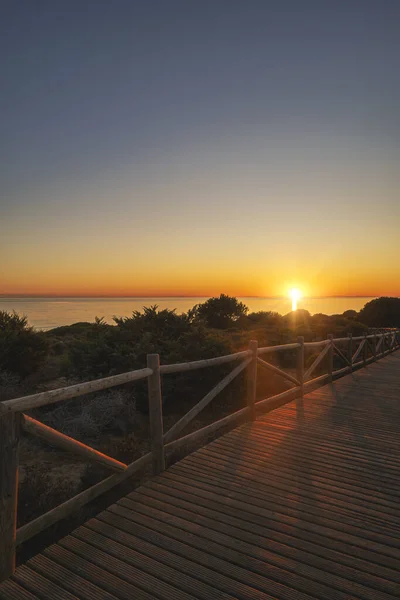 Warm sunset painting the sky over the sea, highlighting a wooden walkway on the serene beach.