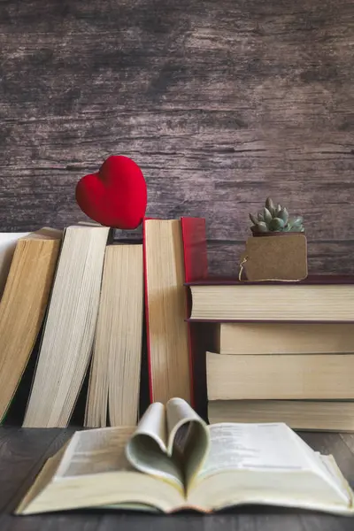 Open book, pages forming a heart, red heart on pile of books. International Book Day, culture, love celebration.