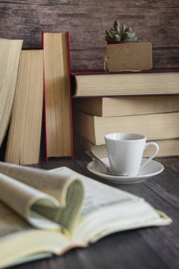 Açık bir kitap, ön planda bardaklar, bir kart ve bir fincan kahve, arka planda yığınla kitap. Uluslararası Kitap Günü, kültür, bilgelik.