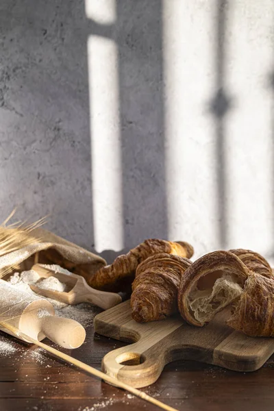 Still life of croissants on top of a wooden board, sack of flour and dowels, front view