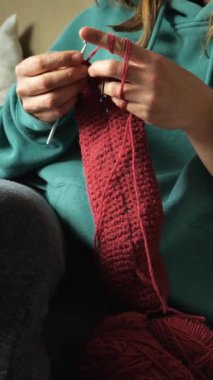 Kafkasyalı genç bir kadının elleri kırmızı iplikle eşarp örüyordu. Oturma odasındaki kanepede oturmak. Dikey video