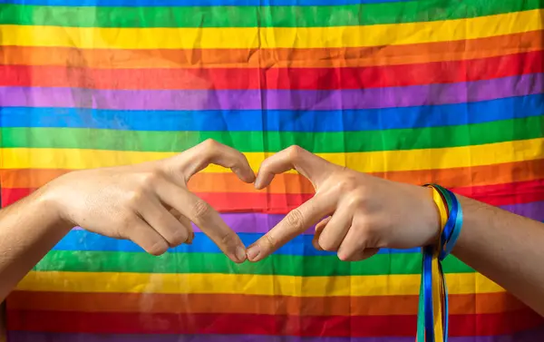 Two hands join to form a heart with LGBT flag background. Concept of gay pride day and love between different races, human beings against discrimination.