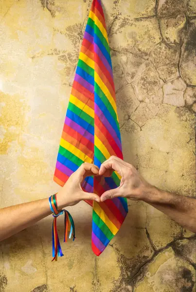 Two hands join to form a heart with LGBT flag background. Concept of gay pride day and love between different races, peace, human beings against discrimination.