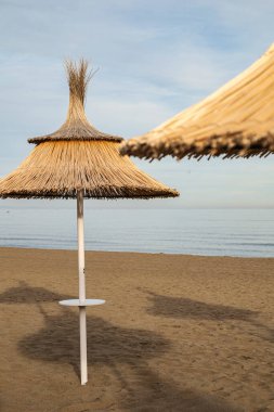 Straw umbrella in the foreground on a beach at sunset, calm and serene environment without people. clipart