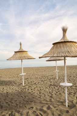 Gün batımında plajda sazdan yapılmış üç şemsiye. İnsansız sakin ve huzurlu bir ortam..