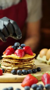Kremalı yaban mersini poz veren adam, ahşap bir tahtada çilek ve çilek, ılık ışık, bar, dikey video