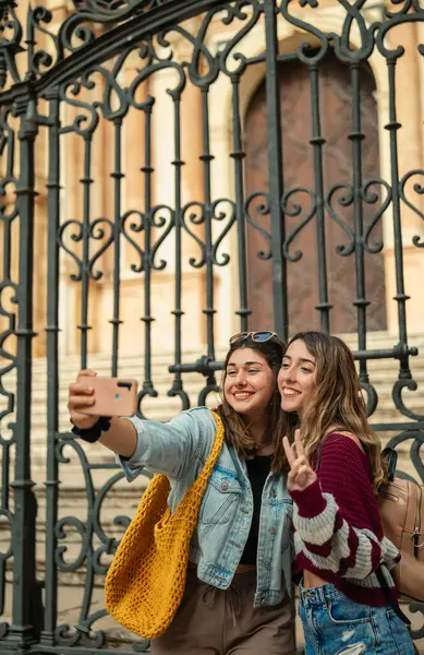 İki Kafkasyalı turist kız gülümseyip Malaga katedralinin önünde selfie çekiyorlar..