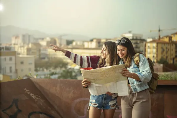 Günlük kıyafetlerle gezen iki beyaz kız Malaga, İspanya 'da bir turizm şehrinin haritasına bakıyor..