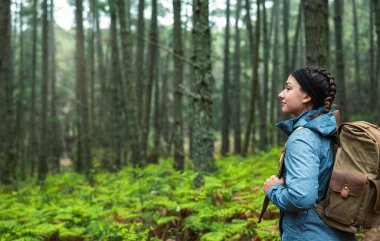 Saç örgüleri ve sırt çantasıyla çam ağaçları ve eğreltiotlarından oluşan bir ormanda büyülenmiş doğa ve sürdürülebilirlik aşkı olan genç bir kız..