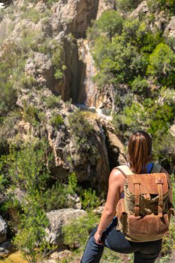 Sırt çantalı bir kız kanyonun tepesinden bir şelaleye bakıyor, turizm, macera ve doğa..