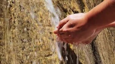 Ön planda, güneşin altında bir şelalede ıslanan ellerin videosu. Tazelik hissi.