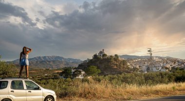 Gün batımında İspanya 'nın iç kesimlerine yapılan bir gezi sırasında uzaktaki tipik bir Endülüs köyüne bakan bir kızın panoramik yatay fotoğrafı..