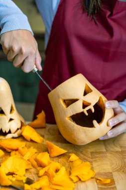 Cadılar Bayramı için dekorasyon yapan yaratıcı genç kız, evde kutlama yapan ve balkabağı oyan bir aile..