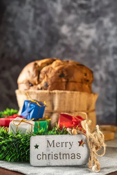 Mutlu bir Noel kartının yakın çekimi, arka planda odaksız bir Panettone süs ve hediyelerle çevrili..