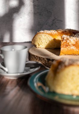 Rosco de Reyes arka planda, ön planda, yanında bir fincan kahveyle odak dışı tatlı bir parça kesilmiş, tipik İspanyol tatlısı, Noel atıştırmalığı. Üç Krallar Günü.