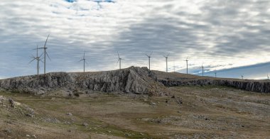 Doğal bir dağ manzarasıyla çevrili, dağların tepesine kurulmuş rüzgar türbinleri yenilenebilir enerji ve doğal çevreyi birbirine bağlıyor..