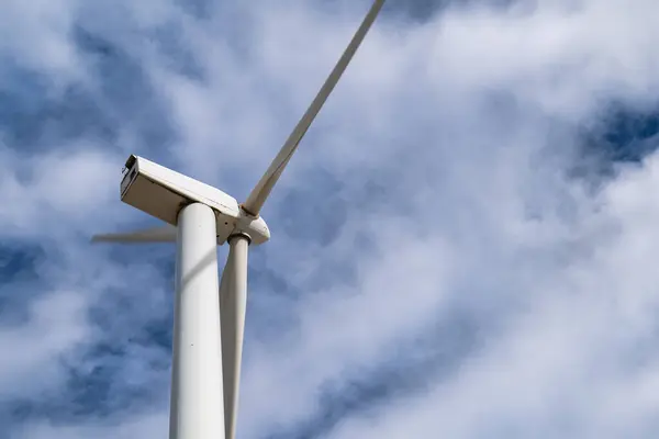 Rüzgâr türbininin hareket halindeki yakın görüntüsü, bulutlar, yenilenebilir enerji ve sürdürülebilirlik ile açık mavi bir gökyüzünün altında dönen bıçakları..