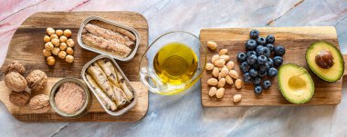 Kalp dostu malzemeler, avokado, fındık, zeytin yağı ve ahşap tahtalarda konserve balık. Sağlık ve beslenme konsepti.