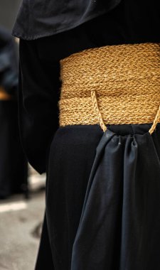 Close-up of a Nazarene dressed in black tunic, highlighting his wide esparto grass belt. Symbolic image of Holy Week in Andalusia, tradition, devotion and sacrifice processions. Symbolism and culture. clipart