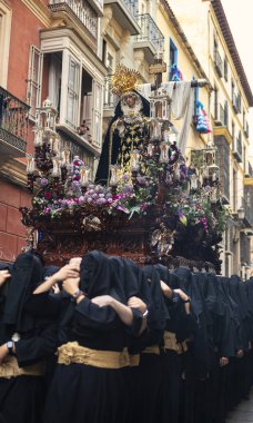 Throne of the Virgin Mary in procession through the streets of Malaga during Holy Week. Virgin holding Jesus' crown of thorns, an expression of suffering and pain. In the background, the cross, religious symbolism of the scene. clipart