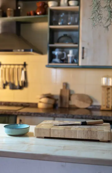 Ahşap kesim tahtası ve tezgahında bıçak olan taşralı bir mutfak. Mutfak aletleri, raflar ve sofra takımlarıyla odaklanma dışı. Sıcak ve rahat bir atmosfer..