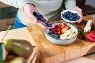 Yaban mersinlerini meyveli kaseye döken ellerin detaylı görüntüsü. Ev yemeği, doğal yemek ve sağlıklı yaşam tarzı..