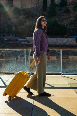 Güneşli bir sabahta Malaga 'da bir Roma tiyatrosunun önünde yürüyen genç bir kız. O, güneş gözlüğü, mor ceket ve yeşil pantolon giyiyor ve çevreyi izlerken sarı bir bavul sürüklüyor.