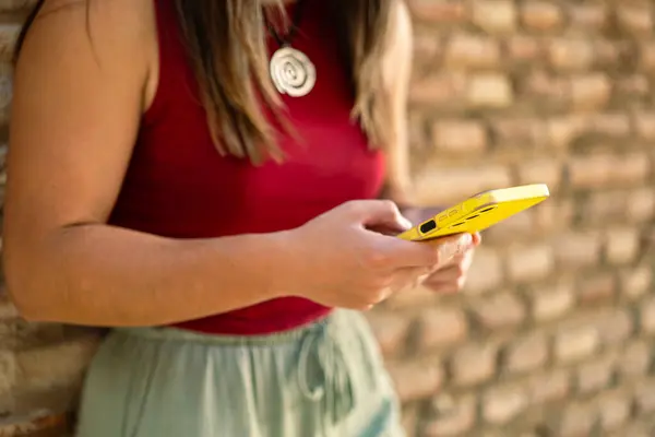 Tuğla duvarın önünde cep telefonu kullanan kadının ayrıntıları, cihaza odaklan. Kopyalama alanı ve sıcak tonların karışımı ile yaratıcı çekim.