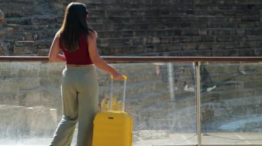 Çantalı ve klasik kameralı genç adam Malaga 'ya doğru yürür, Roma Tiyatrosu' nun fotoğrafını çekmek için durur ve sonra ön taraftan bir fotoğraf daha çeker. Sert ışık ve uzun gölgeler.