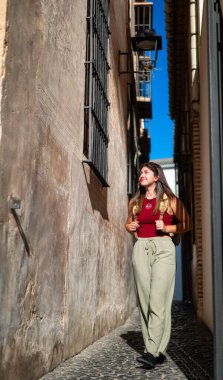 Klasik sırt çantalı bir kız Malaga 'nın tarihi merkezindeki bir ara sokaktan çıkarken kameraya doğru yürüyor. Kentsel ve kültürel çevrede sessiz ve ilginç ifade.