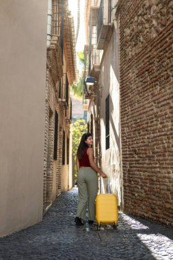 Sarı bavullu bir kız Malaga şehir merkezindeki ortaçağ geçidinde yürüyor. Tuğla duvarlar ve eski alçılarla dolu bir ortamda gülümsüyor..