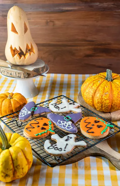 Ev yapımı Cadılar Bayramı şekilli kurabiyelerin olduğu yere götür. Etraflarında balkabakları olan bir ızgaradalar. Odaklanma dışı arka plan loş ışık ve sonbahar havası.