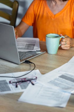 Elinde kahve tutarken dizüstü bilgisayarda yazan kadın. Evdeki dikey sahne, doğal ışık ile sıcak ve rahat atmosfer.