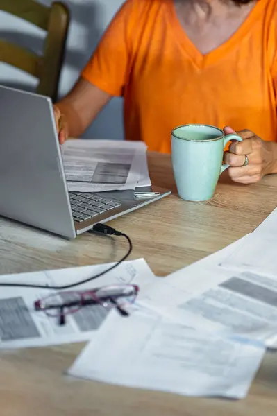 Elinde kahve tutarken dizüstü bilgisayarda yazan kadın. Evdeki dikey sahne, doğal ışık ile sıcak ve rahat atmosfer.