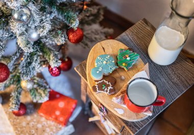 Bir Noel ağacının yanında küçük bir masa, bir sürahi süt, kırmızı bardak ve ev yapımı kurabiyeyle birlikte Noel içeceği ayrıntıları..