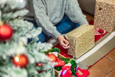 Yatay fotoğraf. Noel kağıdına sarılı birçok hediye süslenmiş ağacın önünde dinleniyor. Detayları ve şenlikli atmosferi yakalıyor..