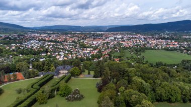 Expansive aerial view of a picturesque European town of Saalfeld Thuringia, featuring lush greenery, sprawling landscapes, and distant rolling hills under a cloudy sky clipart