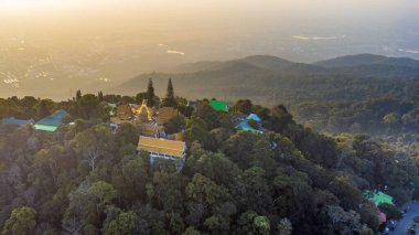 Kuzey Tayland 'daki Chiang Mai şehrine bakan bir orman dağında gün batımında parlayan Budist tapınağının hava manzarası..