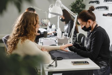 Manikür salonu. Modern güzellik salonundaki kadınlar için koruyucu maske takan profesyonel bir manikürcü. Güzellik endüstrisi konsepti. Cilalama lambası