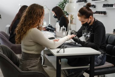 Kuaförde manikür yapıyor. Profesyonel kuaförde müşteri çivileri üzerinde çalışan kadın manikürcü. Meslek konsepti. Güzel yeşil modern stüdyodaki müşteriler 