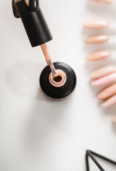 stock image Gel lacquer standing at table. Close up view of black bottle standing at the white table, hand holding brush at the nail salon, color samples. Beauty routine concept. Top view