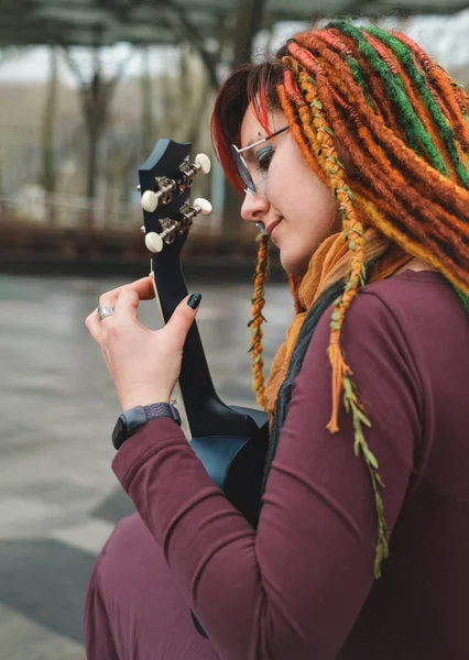 30多岁的时候 一个有趣的自由嬉皮士女人 带着可怕的头发坐在路旁的长板上弹奏吉他 秀发艳丽的女性享受户外积极的生活方式 弹奏音乐 — 图库照片